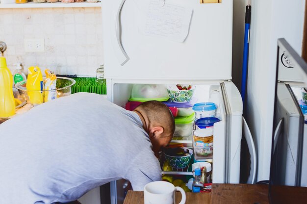 Giovane nella sua cucina di casa sporgendosi in cerca di ingredienti nel frigorifero per cucinare il pranzo