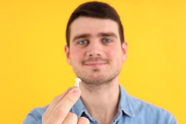 Young man hold hearing aid on yellow background