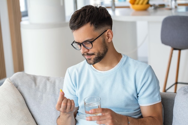 Young man hold pills and glass of water in his hands Concept of healthcare and medicine patient take daily dose of prescribed medicament feel sick antibiotics painkillers or antidepressants Close up