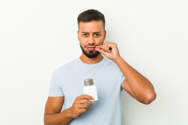 Young man holding an after shave cream with fingers on lips keeping a secret