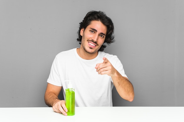 Young man holding an aloe vera bottle cheerful smiles pointing to front.