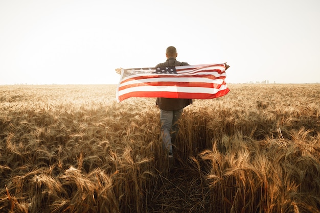 写真 麦畑に立っている間、背中にアメリカ国旗を保持している若い男