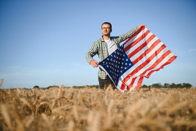 麦畑に立ってアメリカの国旗を保持している若い男