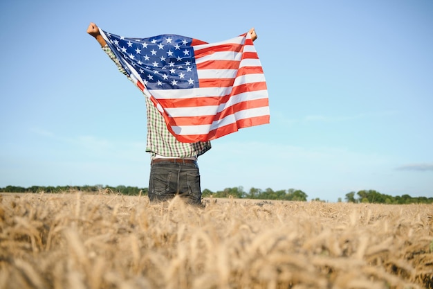 麦畑に立ってアメリカの国旗を保持している若い男