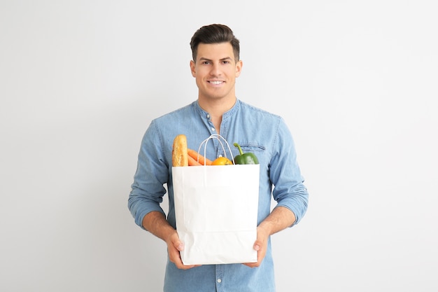 Young man holding bag with food on light background