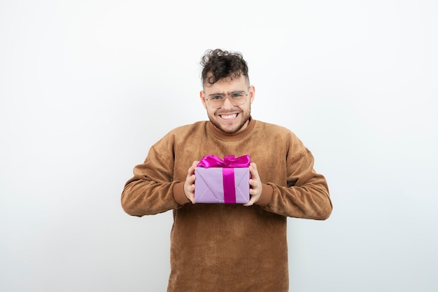 Young man holding big present gift box against white wall . 