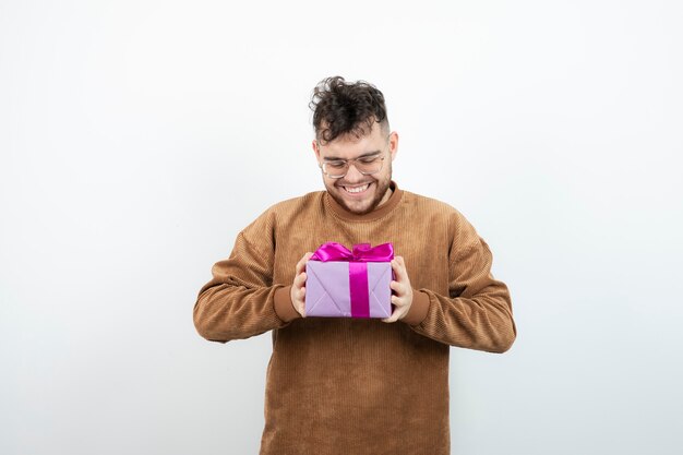 Young man holding big present gift box against white wall . 