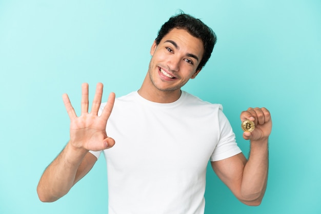 Young man holding a Bitcoin over isolated blue background happy and counting four with fingers