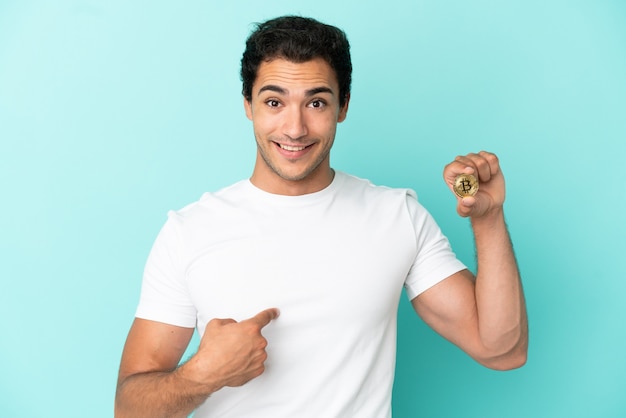 Young man holding a Bitcoin over isolated blue background with surprise facial expression