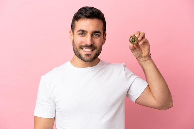 Young man holding a Bitcoin isolated on pink background looking side