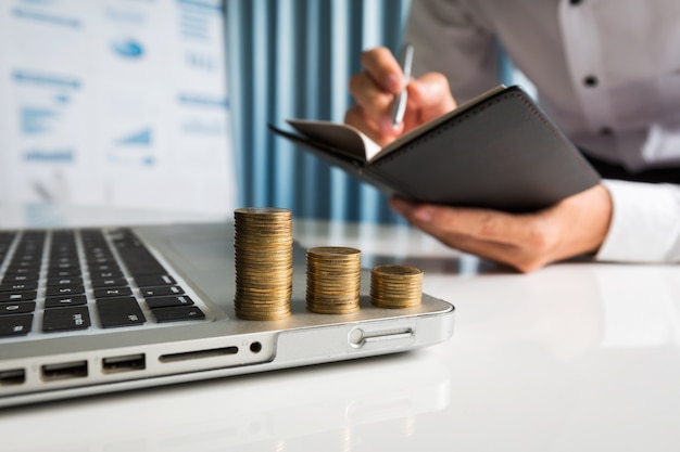 Young man holding black notebook with coins on laptop.