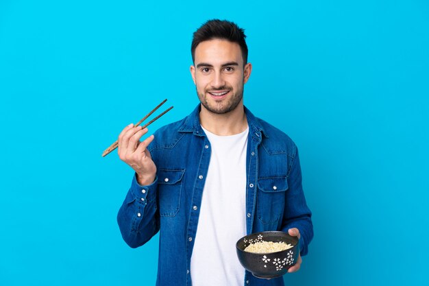 Young man holding a bowl of noodles over isolated wall