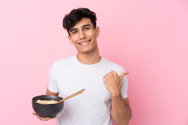 Young man holding a bowl of noodles over isolated wall