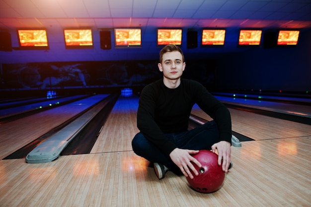 Young man holding a bowling ball sitting against bowling alleys with ultraviolet light.