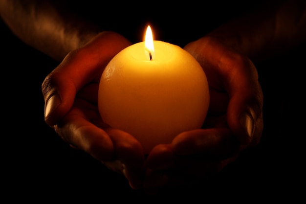 Young man holding burning candle in darkness