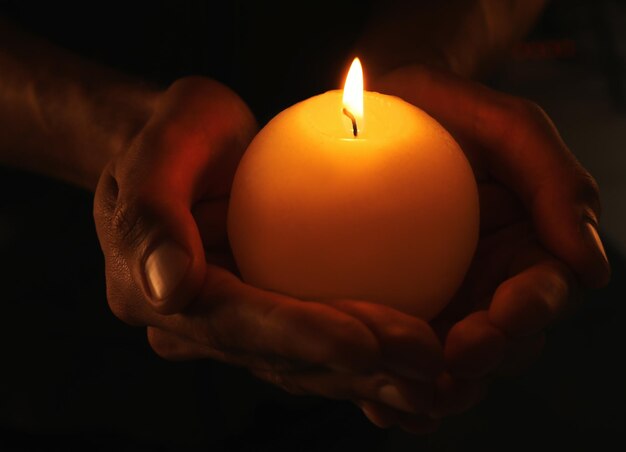 Young man holding burning candle in darkness