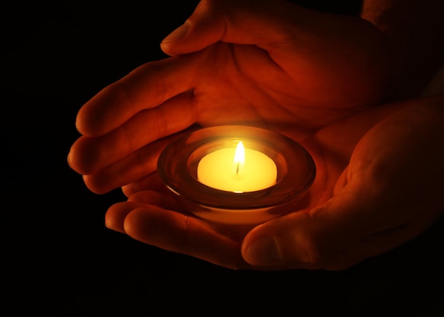 Young man holding burning candle in darkness