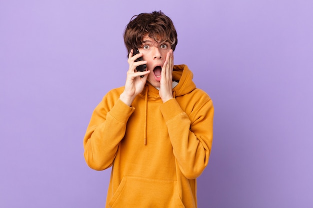 Young man holding a cell feeling shocked and scared