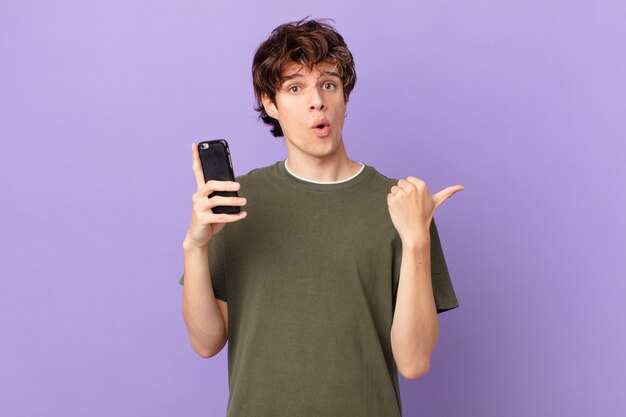 Young man holding a cell looking astonished in disbelief