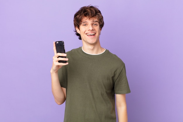 Young man holding a cell looking happy and pleasantly surprised