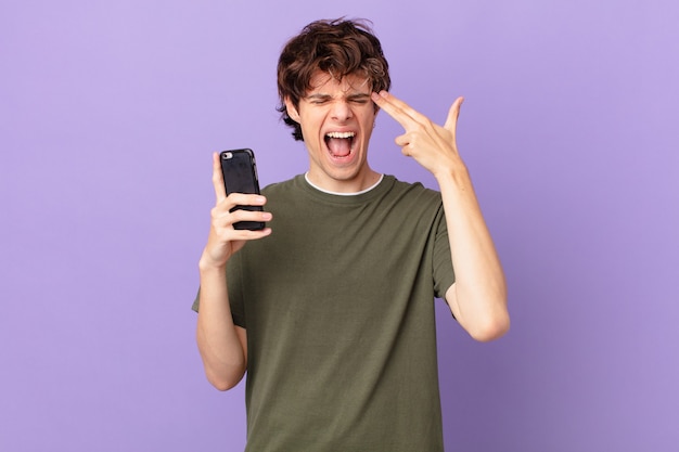 Young man holding a cell looking unhappy and stressed, suicide gesture making gun sign