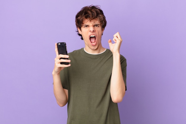 Young man holding a cell shouting aggressively with an angry expression