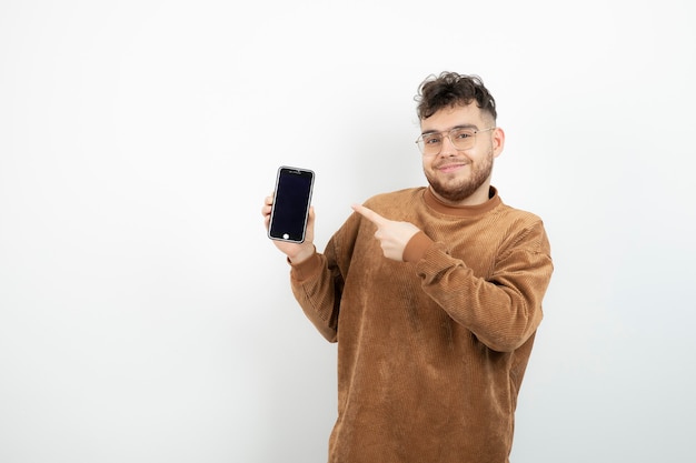 young man holding cellphone over white wall. 