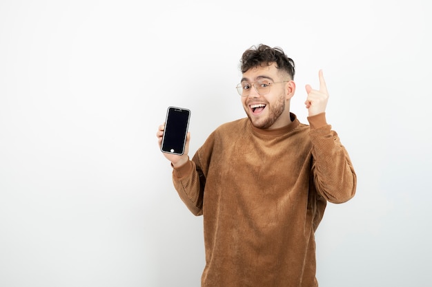 young man holding cellphone over white wall. 