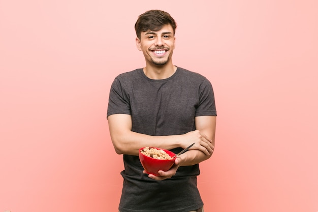 Young man holding a cereal bowl smiling confident with crossed arms