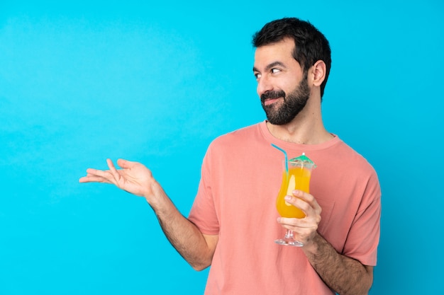 Young man over holding a cocktail over blue extending hands to the side for inviting to come