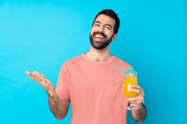 Young man over holding a cocktail over isolated blue wall smiling