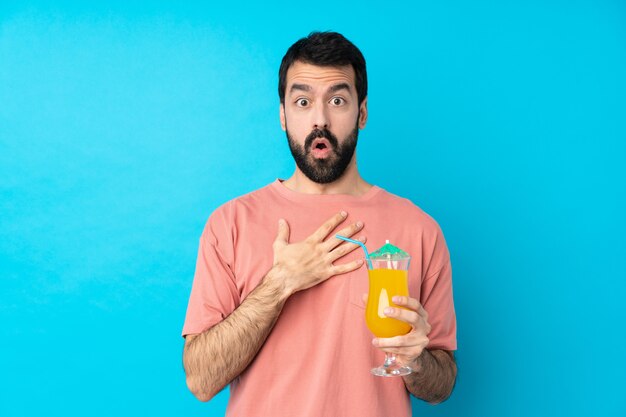 Young man over holding a cocktail over isolated blue wall surprised and shocked while looking right