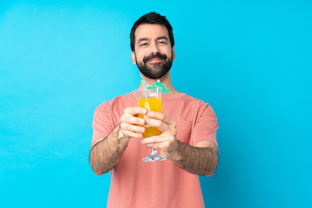 Young man over holding a cocktail over isolated blue wall