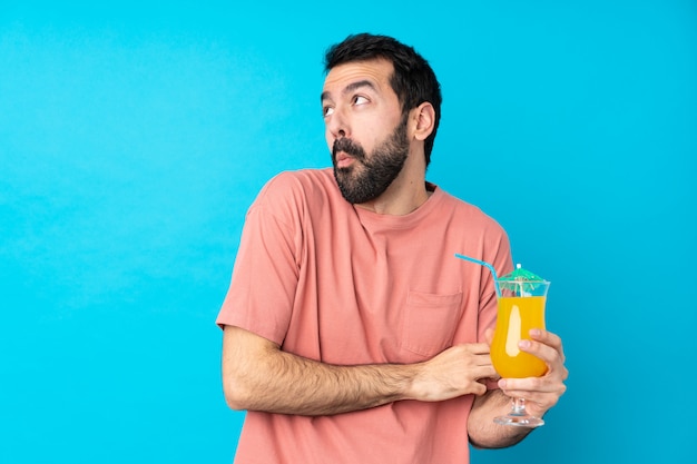 Young man over holding a cocktail over isolated blue