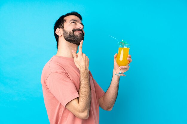 Young man over holding a cocktail over isolated blue