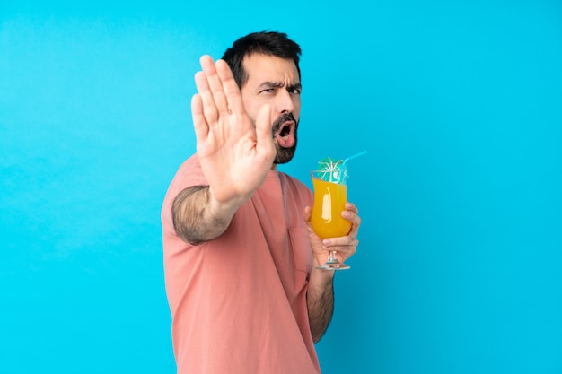 Young man over holding a cocktail making stop gesture and disappointed