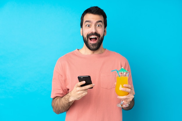 Young man over holding a cocktail surprised and sending a message