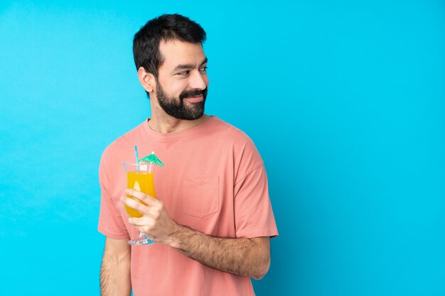 Young man over holding a cocktail with arms crossed and happy