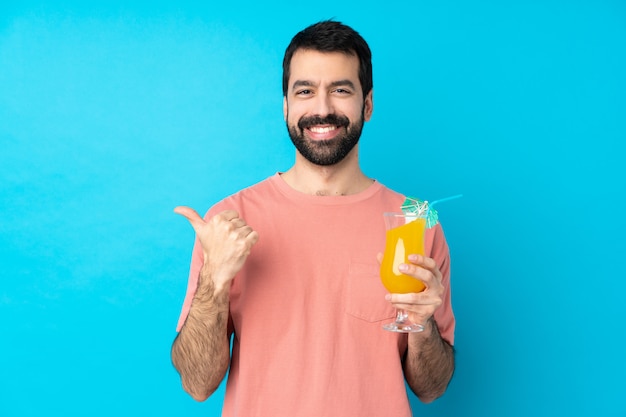 Young man over holding a cocktail with thumbs up gesture and smiling