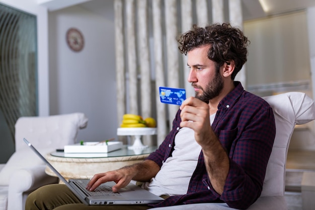 Young Man holding credit card and computer laptop entering data for web-site form, going to pay for online order. People, lifestyle, modern technologies and e-commerce concept