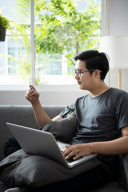 Young man holding credit card and using laptop computer for shopping online at home.