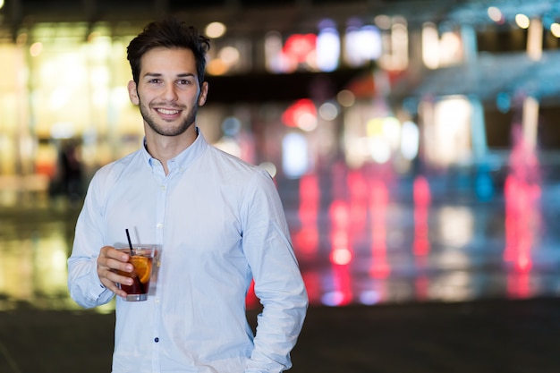 Young man holding a drink at a night club outdoor