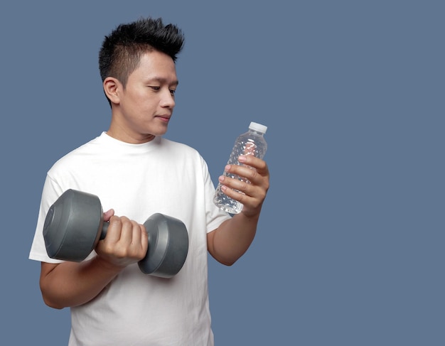 Young man holding dumbbells and bottled water isolated on plain background