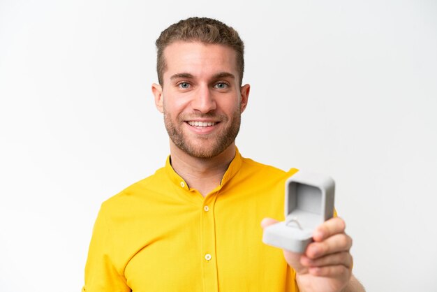 Young man holding a engagement ring isolated on white background with happy expression