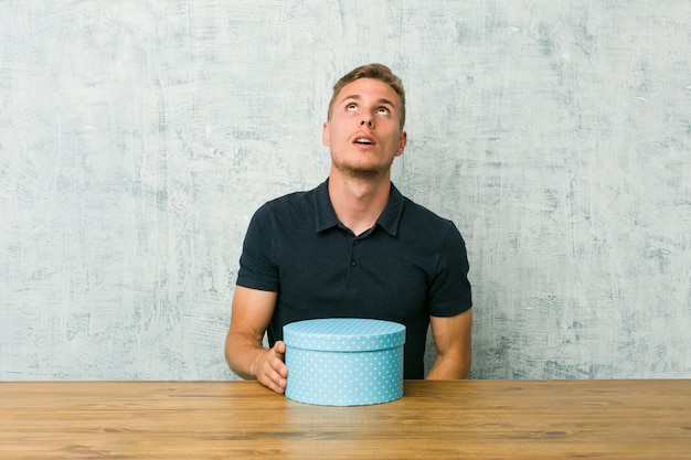 Young man holding a gift box on a table tired of a repetitive task