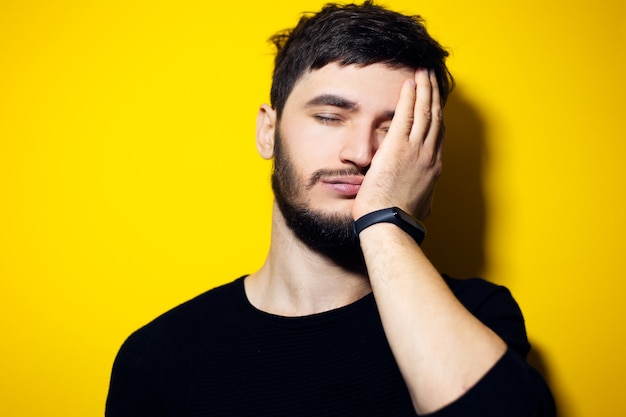 Young man, holding hand on face, feeling tired, wall of yellow color.