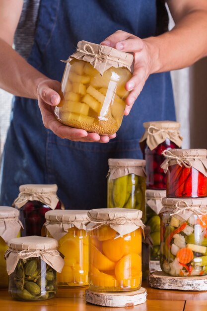 Young man holding in hands jars with homemade preserved and fermented food, pickled and marinated. Harvest preservation, local produce from farmers