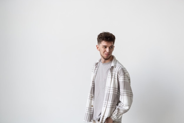 Young man holding hands in pockets and looking at camera while standing against white background