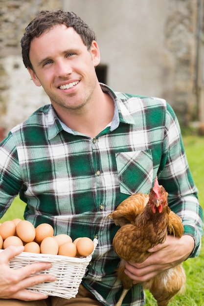 Photo young man holding his chicken and basket of eggs