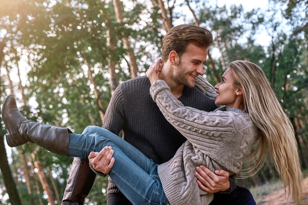 Young man holding his girlfriend on hands in autumn forest